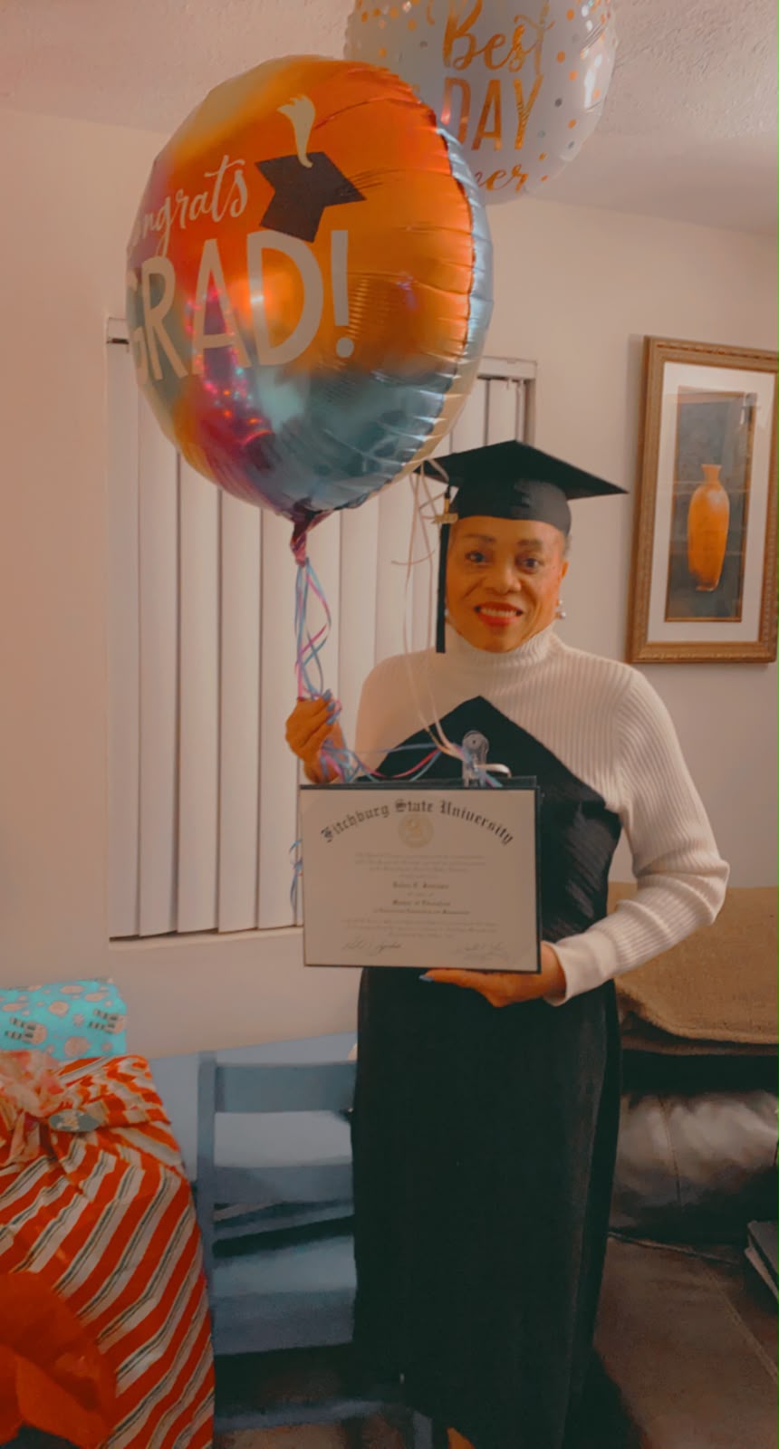 Debra in cap and gown holding her university diploma on graduation day